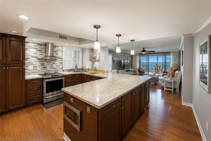 Gourmet kitchen featuring a large island with a stone-finish countertop, rich wood cabinetry, stainless steel appliances, and a mosaic tile backsplash