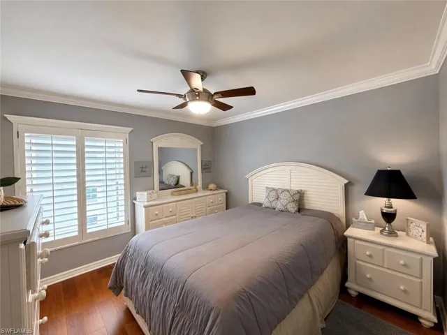 Bedroom featuring wood-finish flooring, plantation shutters, crown molding, a ceiling fan with integrated lighting, and neutral wall tones