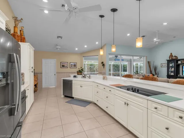 Kitchen featuring appliances with stainless steel finishes, vaulted ceiling, light tile patterned floors, white cabinetry, and pendant lighting