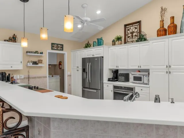 Kitchen with white cabinets, stainless steel appliances, hanging light fixtures, and a breakfast bar area
