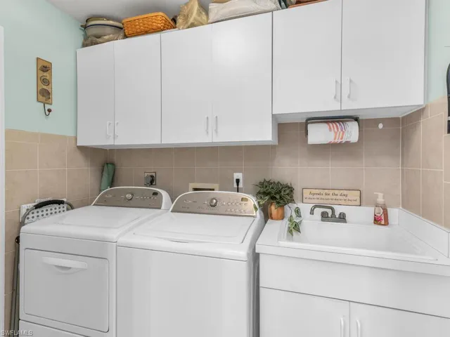 Clothes washing area with tile walls, sink, independent washer and dryer, and cabinets