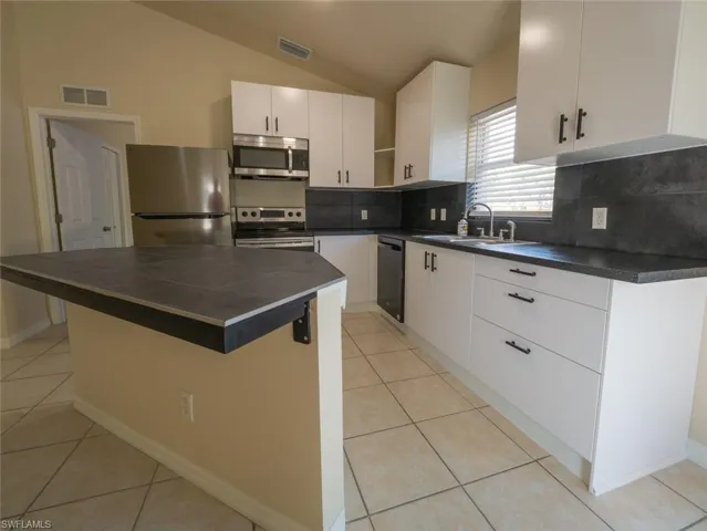 Kitchen with sink, a center island, lofted ceiling, white cabinets, and appliances with stainless steel finishes