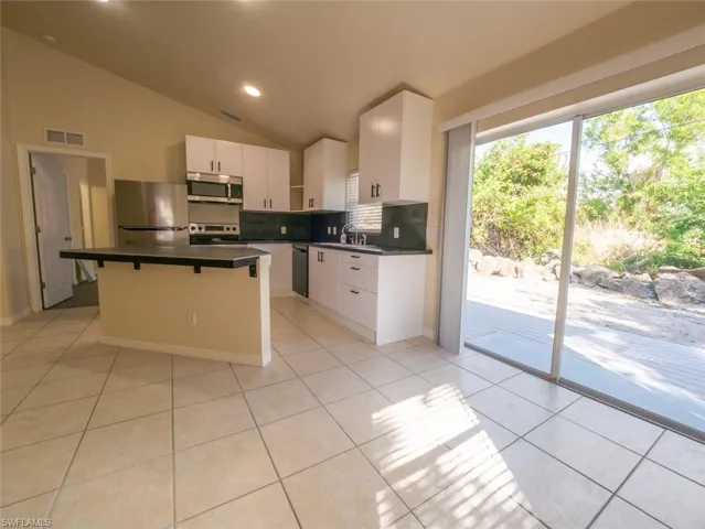 Kitchen featuring vaulted ceiling, light tile patterned floors, appliances with stainless steel finishes, a kitchen island, and white cabinetry