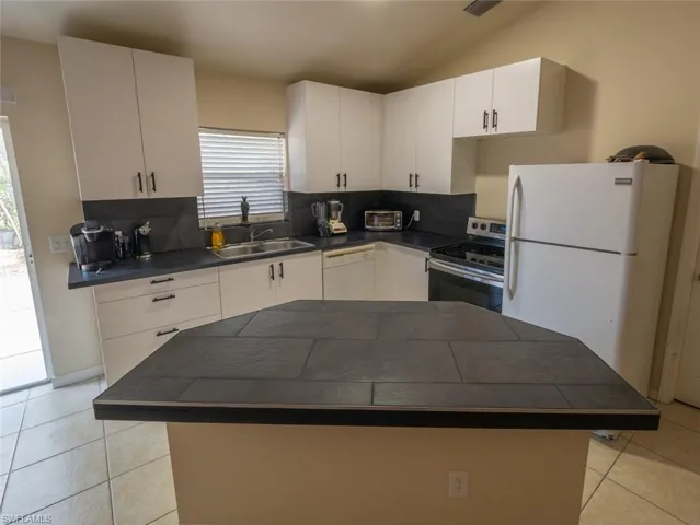 Kitchen with decorative backsplash, white appliances, vaulted ceiling, sink, and white cabinets