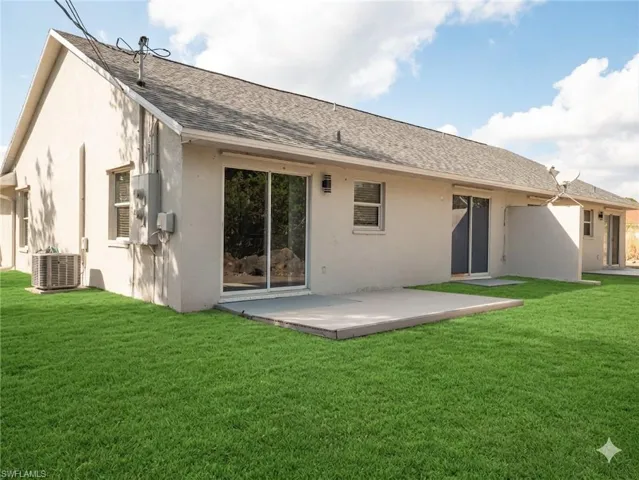 Rear view of property featuring roof with shingles, a yard, stucco siding, and a patio