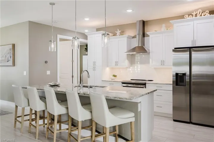 Kitchen with appliances with stainless steel finishes, decorative backsplash, wall chimney exhaust hood, a kitchen bar, and recessed lighting