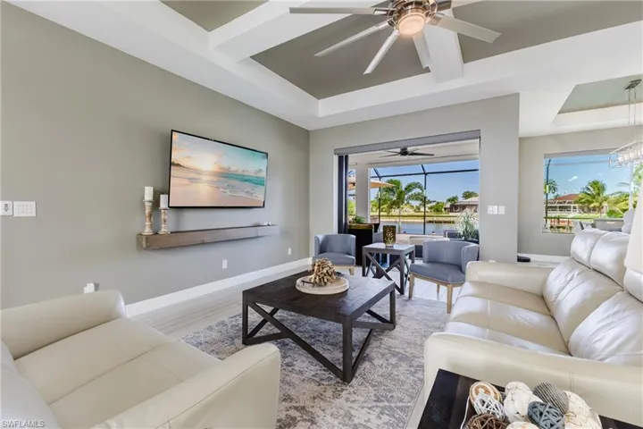 Living room featuring wood finished floors, a tray ceiling, a sunroom, and ceiling fan