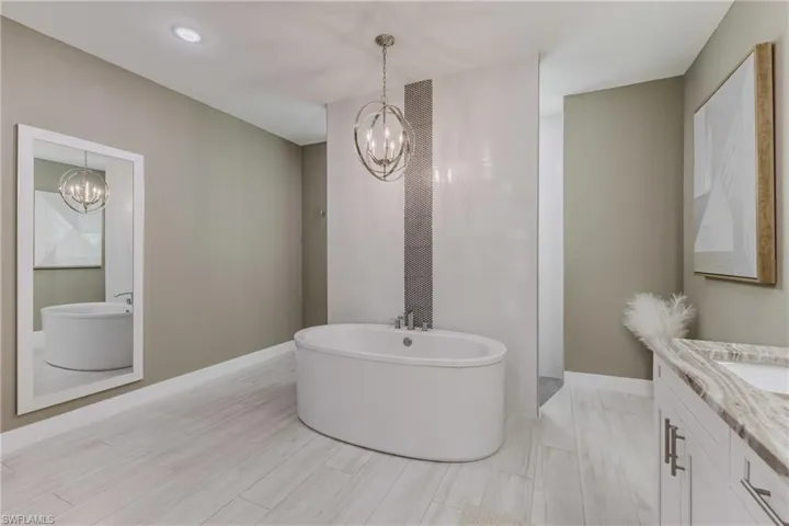 Bathroom with a chandelier, a soaking tub, vanity, and recessed lighting