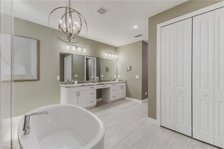 Full bathroom featuring a closet, a freestanding tub, double vanity, recessed lighting, and a chandelier
