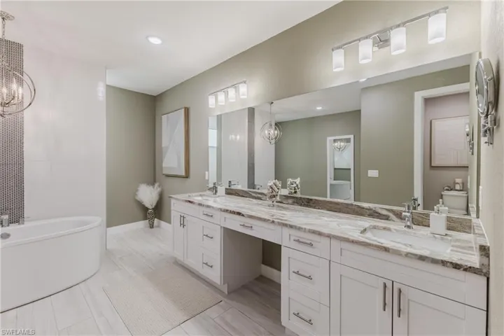 Full bathroom featuring a chandelier, a soaking tub, double vanity, and recessed lighting