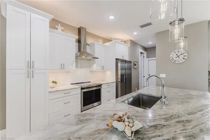 Kitchen with stainless steel appliances, light stone counters, wall chimney range hood, white cabinets, and recessed lighting
