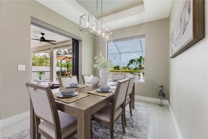 Dining space featuring light wood finished floors, a ceiling fan, a textured wall, a chandelier, and a tray ceiling