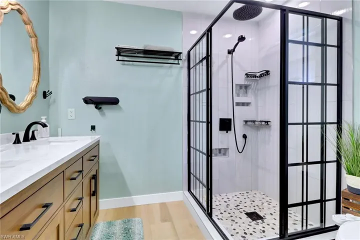 Bathroom with double vanity, a shower stall, and light wood-type flooring