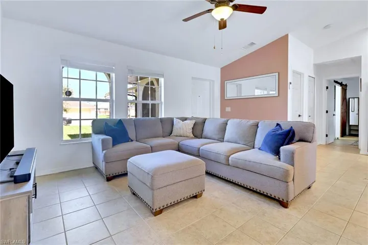 Living room featuring lofted ceiling, a barn door, light tile patterned floors, and ceiling fan