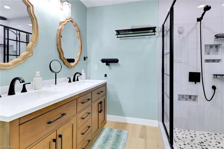Full bath featuring a shower stall, double vanity, and light wood finished floors