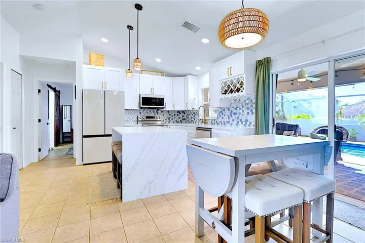 Kitchen with backsplash, appliances with stainless steel finishes, white cabinets, light tile patterned flooring, and light stone countertops
