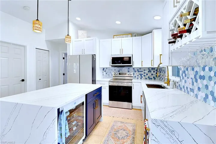 Kitchen with light stone counters, beverage cooler, decorative backsplash, white cabinetry, and white appliances