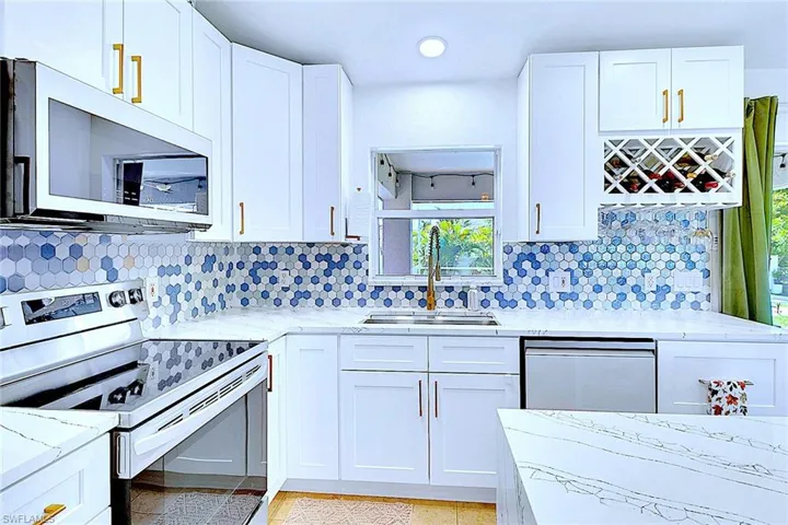 Kitchen featuring stainless steel appliances, backsplash, white cabinets, light stone counters, and recessed lighting