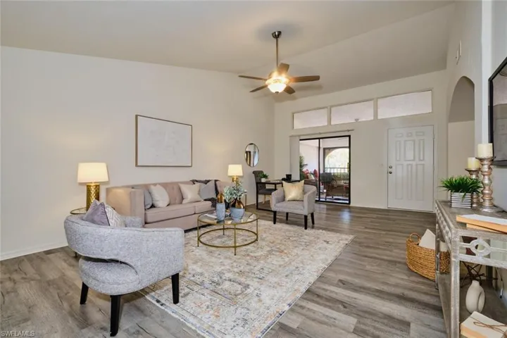Spacious living area featuring vaulted ceilings, wood-finish flooring, a ceiling fan with integrated lighting, and a sliding glass door providing exterior access