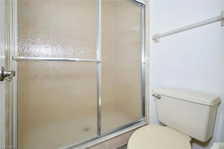 Shower enclosure with textured glass doors, brushed nickel handle, and a tan toilet