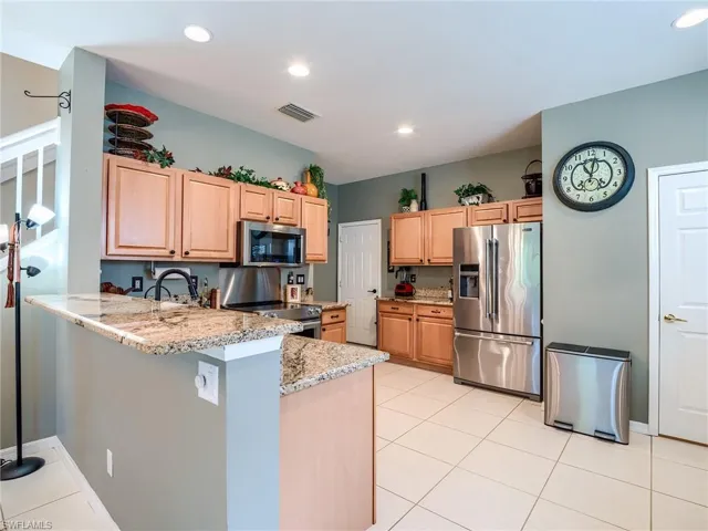 Kitchen featuring light tile patterned floors, kitchen peninsula, light stone counters, stainless steel appliances, and light brown cabinetry