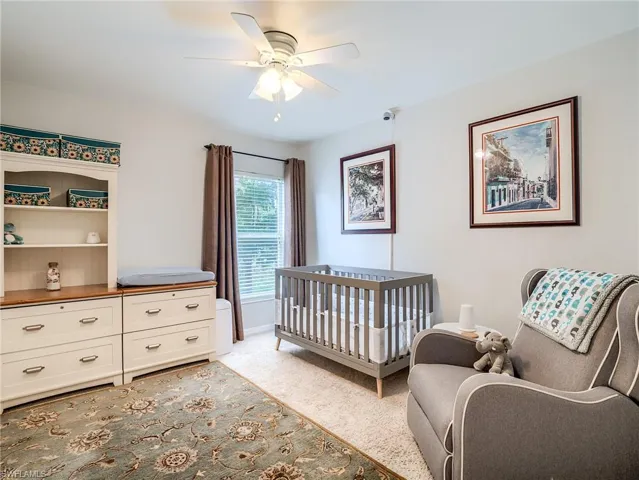 Bedroom with light colored carpet, a nursery area, and ceiling fan