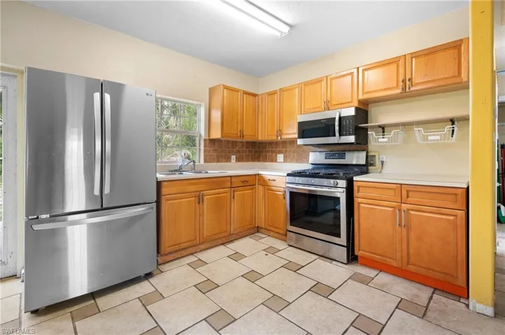 Kitchen with light countertops, tasteful backsplash, a sink, stainless steel appliances and brown cabinetry