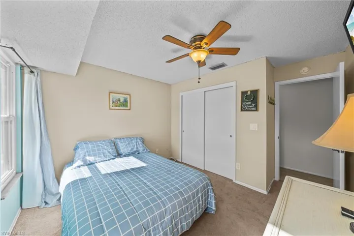 Bedroom featuring light colored carpet, ceiling fan, a closet, and a textured ceiling