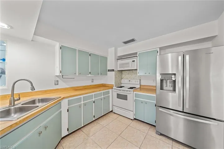 Kitchen featuring white appliances, tasteful backsplash, light tile patterned floors, and green cabinets