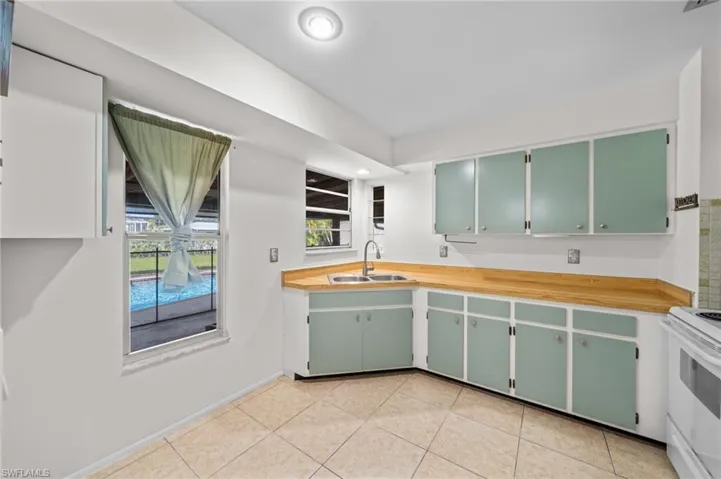 Kitchen with green cabinetry, electric range, light tile patterned floors, and butcher block counters
