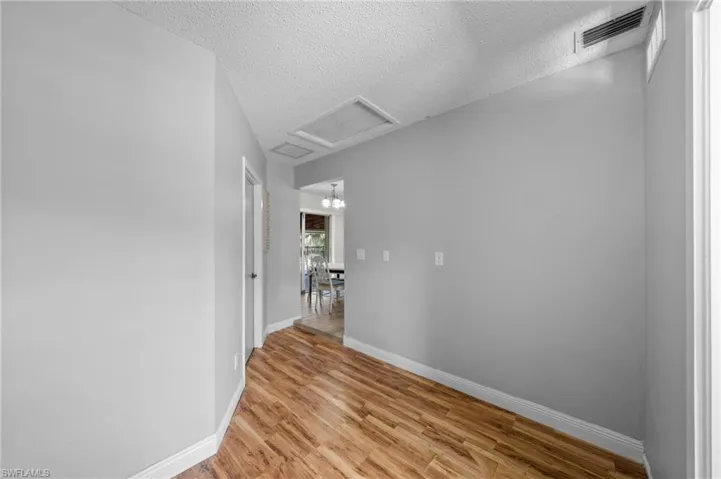 Hall featuring light wood finished floors, a textured ceiling, a chandelier, and attic access