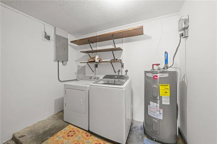 Laundry room featuring water heater, a textured ceiling, electric panel, and independent washer and dryer
