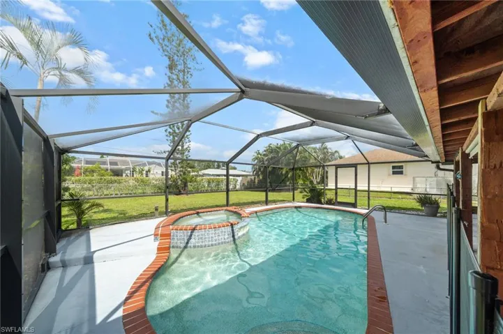 View of pool featuring a patio area, a lawn, a sunroom, and a pool with connected hot tub