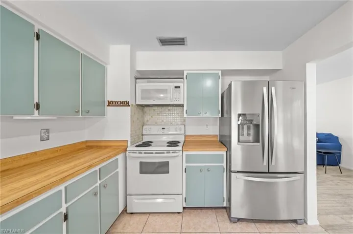 Kitchen with white appliances, decorative backsplash, light countertops, and green cabinets