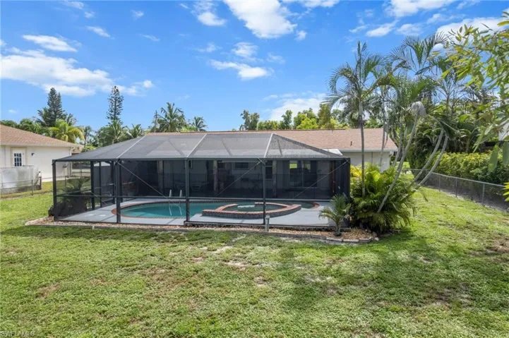Rear view of house with a fenced backyard, a sunroom, and a pool with connected hot tub