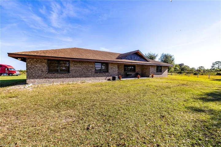Rear view of property featuring a lawn, brick siding, and a shingled roof
