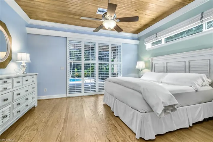 Primary Bedroom features 9'8" ceilings, 6" base and crown moldings, pocketing planation shutters, cypress wood ceilings, transom window for additional light...sliders leading out to pool deck area and natural oak floors.
