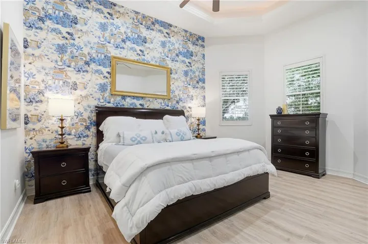 Bedroom with light wood finished floors, wallpapered walls, ceiling fan, and crown molding