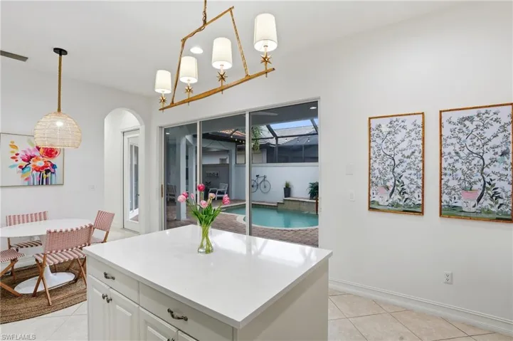 Kitchen featuring white cabinetry, light tile patterned flooring, decorative light fixtures, a center island, and light stone counters