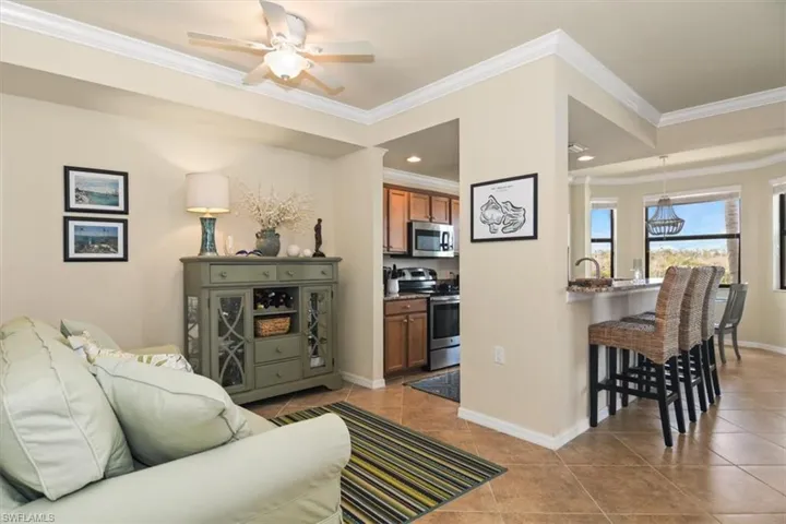 Living room featuring ceiling fan, crown molding, and light tile patterned floors