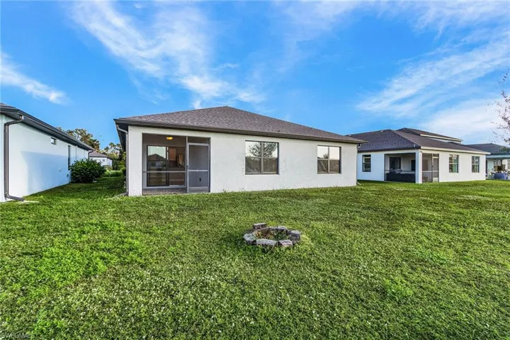 Rear view of house with a yard, stucco siding, a sunroom, and an outdoor fire pit