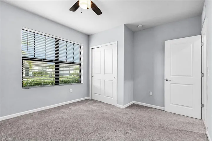 Guest bedroom with large window featuring light colored carpet, a ceiling fan, and a closet