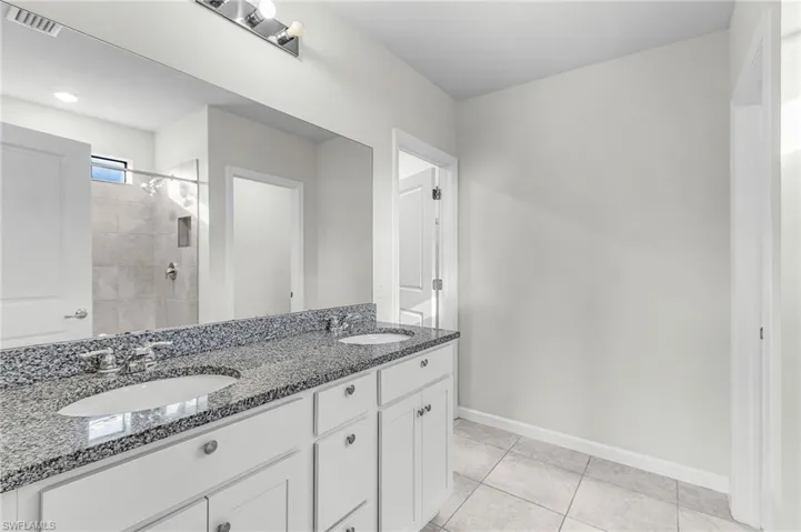 Bathroom with double vanity, light tile patterned flooring, and tiled shower