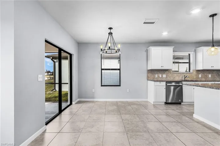 Kitchen featuring a chandelier, tasteful backsplash, white cabinets, stainless steel dishwasher, and granite counters