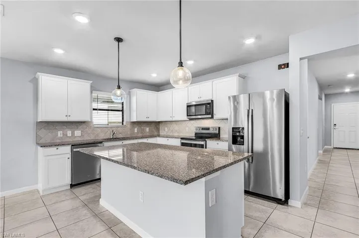 Kitchen featuring stainless steel appliances, granite counters, pendant lighting, white cabinetry, and a center island