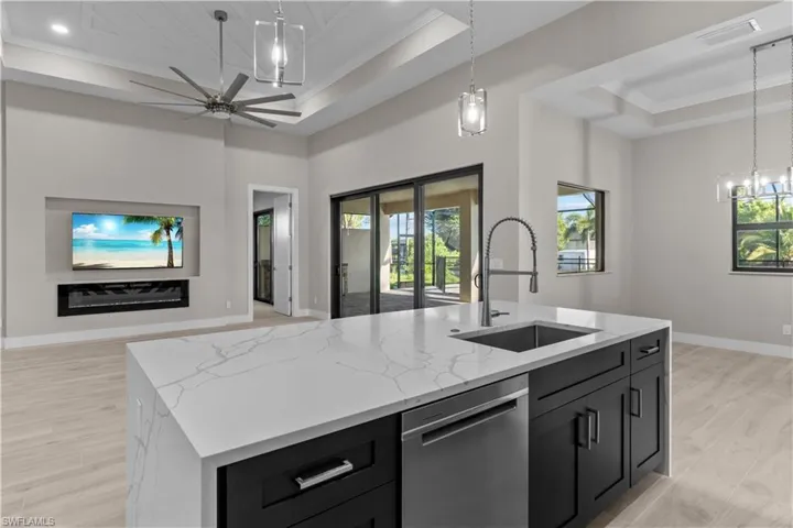 Kitchen featuring dishwasher, a tray ceiling, sink, a center island with sink, and plenty of natural light
