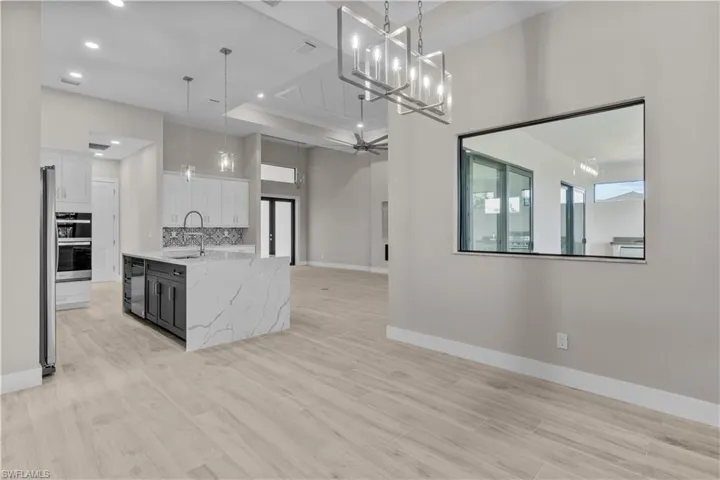 Kitchen with tasteful backsplash, white cabinets, ceiling fan with notable chandelier, light hardwood / wood-style floors, and hanging light fixtures