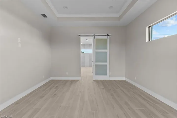 Masterbed room featuring a raised ceiling, light hardwood / wood-style flooring, a barn door, and ornamental molding