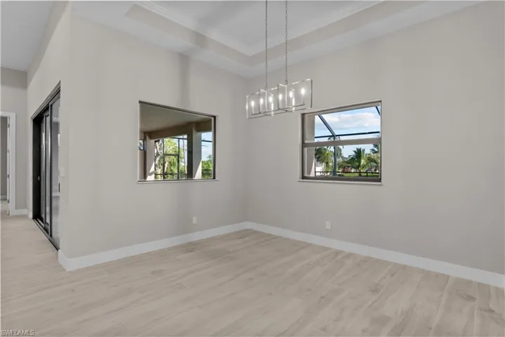 Dinin room with a chandelier, a raised ceiling, light wood-type flooring, and plenty of natural light