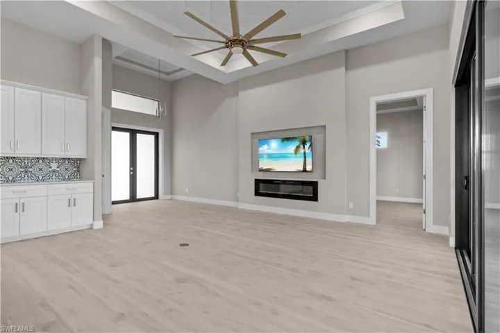 Unfurnished living room with french doors, ceiling fan, a high ceiling, light wood-type flooring, and a tray ceiling